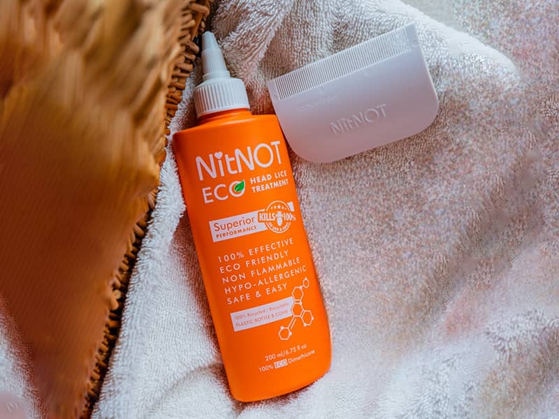 An orange bottle of NitNOT Eco head lice treatment and a white nit comb rest on a white towel—perfect for busy parents, like those managing a top SEO agency UK, seeking effective solutions. seo agency london